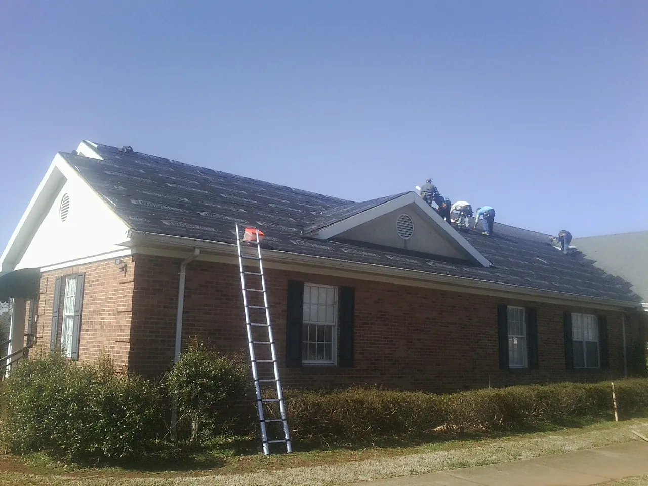 Crew tearing shingles off a brick ranch roof with a ladder set — Metal Roof Repair work by our crew in Pittsburg