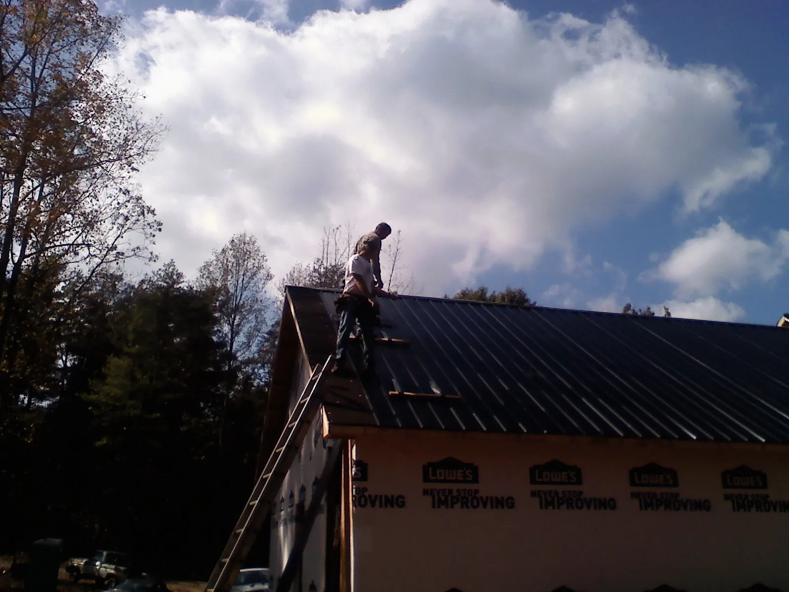 Roofer fastening dark metal panels high against a cloudy sky, from a Roof Inspection job in Pittsburg